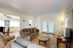 A living room with a sofa, armchairs, a coffee table, a television, and a ceiling fan. - Long Island Village 621 Sand Dollar (Port Isabel)