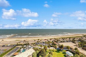A coastal hotel with a parking lot, beach view, and palm trees. - San Luis 14 - Beachfront Resort, Steps to Sand (Galveston)
