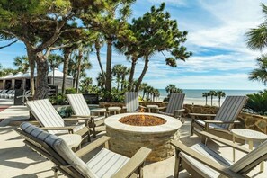 A beachside lounge area with lounge chairs, a stone fire pit, and a view of the ocean. - San Luis 14 - Beachfront Resort, Steps to Sand (Galveston)