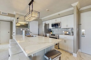 A modern kitchen with a marble countertop, stainless steel appliances, and a hanging light fixture. - San Luis 14 - Beachfront Resort, Steps to Sand (Galveston)
