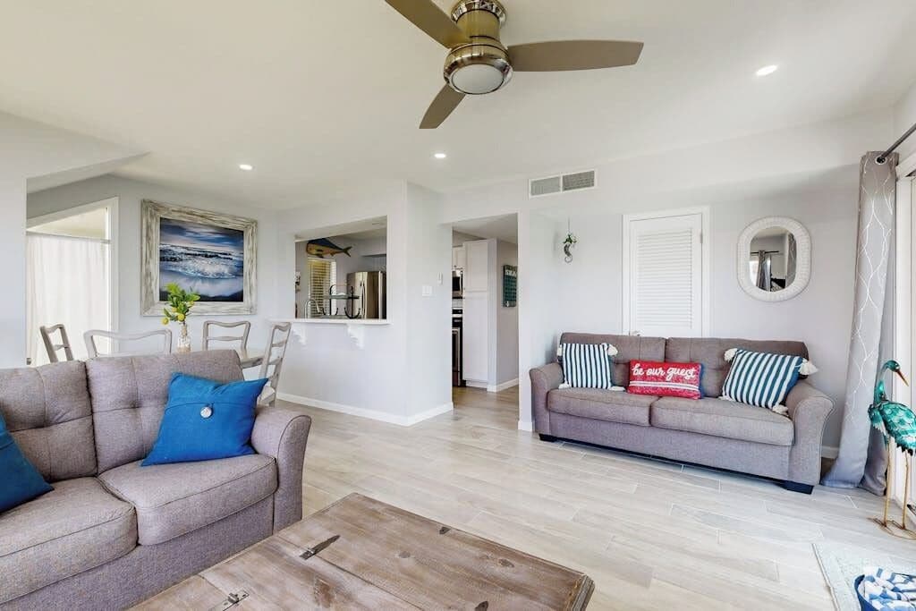 A spacious living area with a grey sofa, a coffee table, and a ceiling fan.