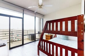 A bedroom with a wooden bunk bed, a ceiling fan, and a view of the city through large windows. - Sunchase IV #525 - Gulf Views, Pools & Sauna (South Padre Island)