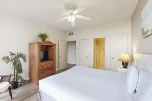 A bedroom with a bed, a ceiling fan, a wooden wardrobe, a television, a nightstand with a lamp, and a potted plant. - Sunchase IV #525 - Gulf Views, Pools & Sauna (South Padre Island)
