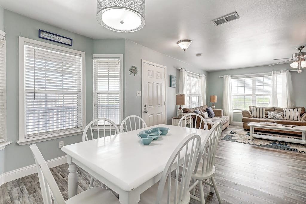 A dining area with a white table and chairs, a kitchen area with a white door, and a living room with a sofa and a coffee table.