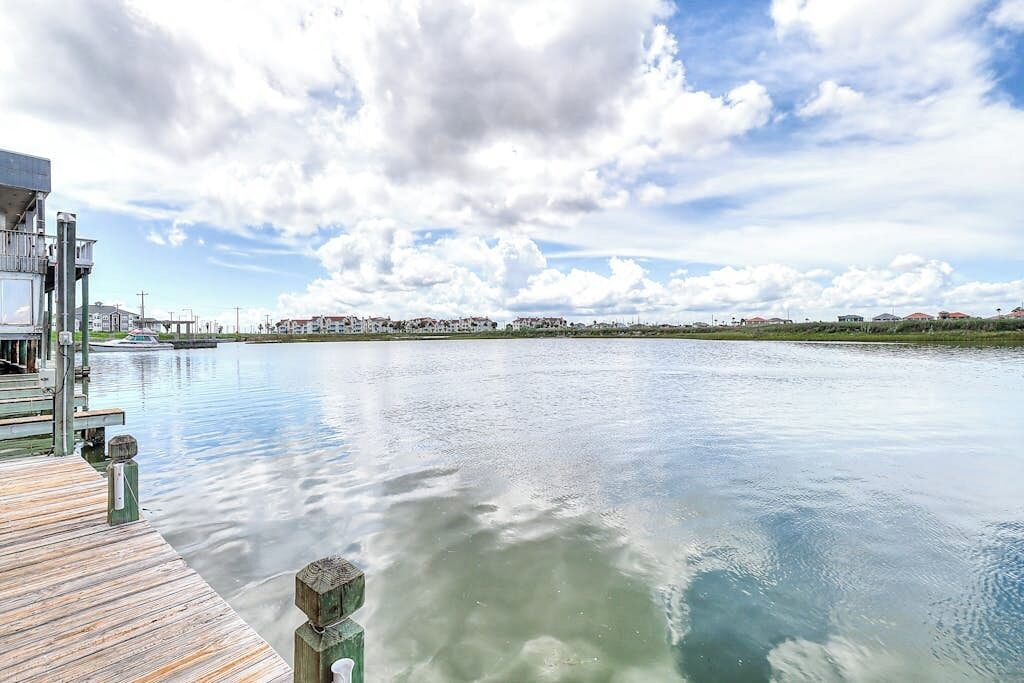 A waterfront property with a dock extending into calm water, a clear sky, and distant buildings.