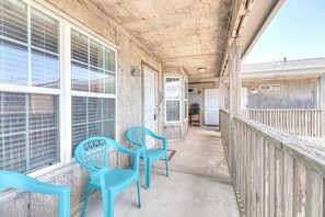 Un espace extérieur abrité, doté d’un sol en béton, de murs en bois et d’une clôture en bois. On y trouve deux chaises en plastique bleues et une petite table.
