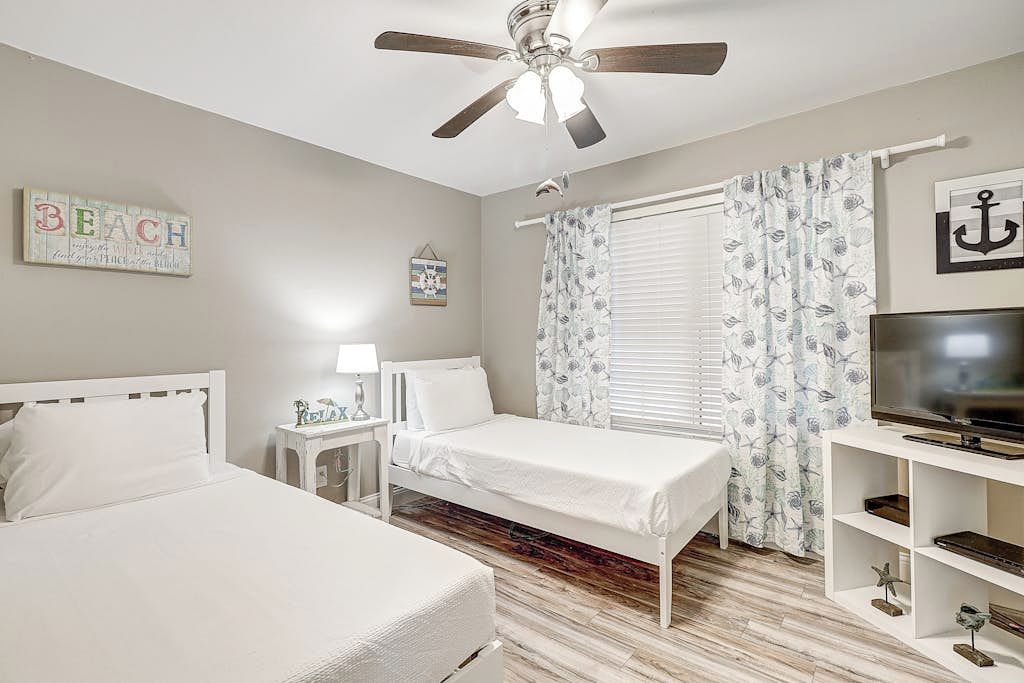 A bedroom with two beds, a ceiling fan, a television, and a window with curtains.