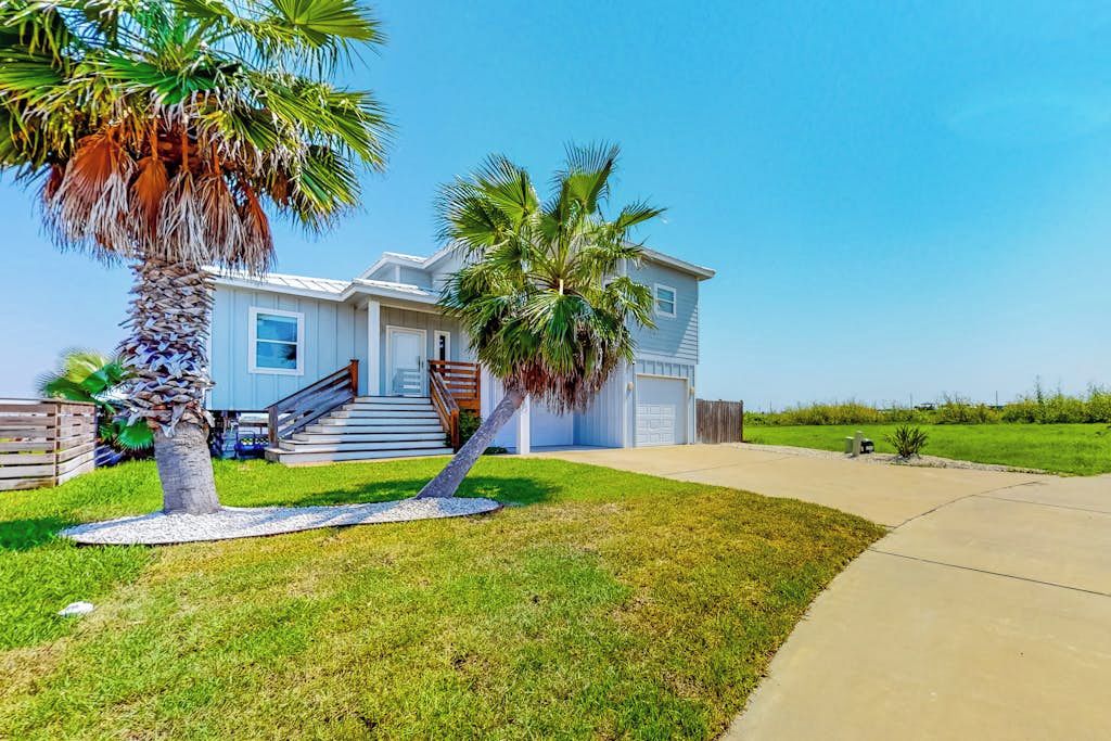 A single-story house with a front porch, a staircase, and a palm tree in the yard.