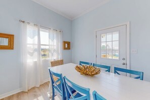 A dining area with a white table, blue chairs, and a decorative centerpiece. - Lilac Sky - Water Views, Pool & Dogs OK (Port Aransas)