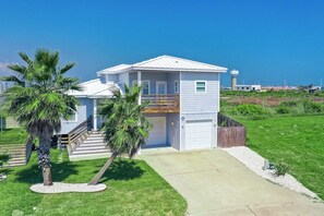 A two-story house with a garage, a staircase, and a small deck. - Lilac Sky - Water Views, Pool & Dogs OK (Port Aransas)