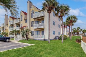 A multi-story residential building with balconies, a parking area, and palm trees. - Beach Club 280 - Pool, Hot Tub, Sauna & Dogs OK (Corpus Christi)