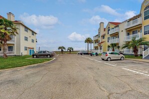 A residential street with multi-story buildings, parked cars, and palm trees. - Beach Club 280 - Pool, Hot Tub, Sauna & Dogs OK (Corpus Christi)
