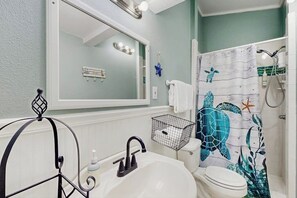 A bathroom with a white sink, a mirror, a shower curtain with a sea turtle design, and a towel rack. - The Seahorse Cottage (Corpus Christi)