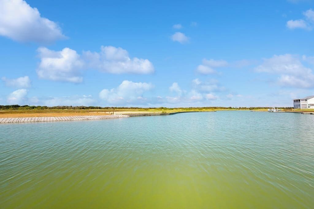 Ruhige Wasserfläche mit blauem Himmel und einem entfernten Gebäude.
