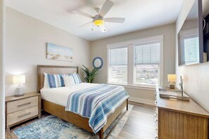 A bedroom with a bed, bedside tables, a ceiling fan, a window with blinds, and a wall-mounted TV. - Waterfront Villa on St Charles Bay (Rockport)