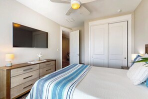 A bedroom with a bed, a dresser, a mirror, a ceiling fan, and a door. - Waterfront Villa on St Charles Bay (Rockport)
