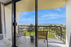A balcony with a view of the ocean, a chair, and a small table. - San Luis Sunshine #631 (Galveston)