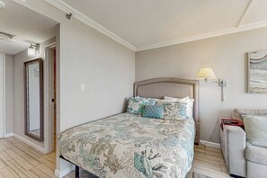 Een slaapkamer met een bed, nachtkastje, lamp en een schilderij aan de muur.