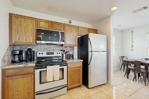 Una cocina con armarios de madera, estufa, refrigerador y un comedor con sillas.