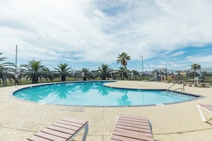 A swimming pool with a sandy deck, surrounded by palm trees and a fence. - Sandpiper Villa - Beach Views, Pool, Dogs OK (Galveston)