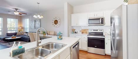 A modern kitchen with stainless steel appliances, a dishwasher, and a dining area with a sofa and coffee table.