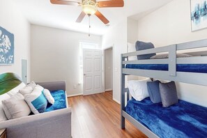Ein Zimmer mit Etagenbett, Schlafsofa, Deckenventilator und einer Tür.