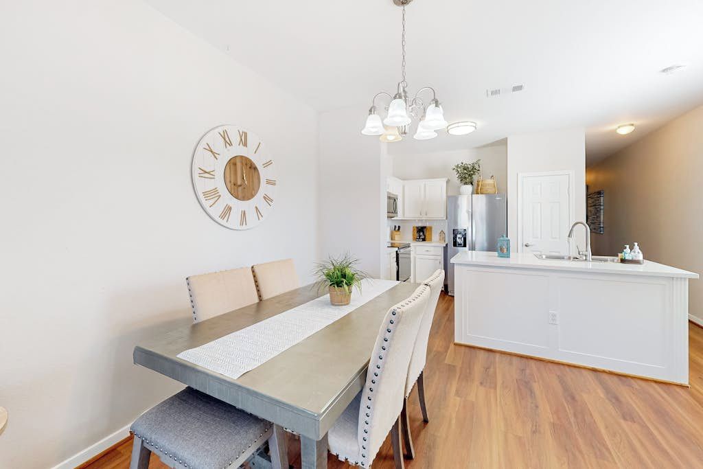 Une cuisine moderne avec des meubles blancs, un îlot central et un coin repas comprenant une table et des chaises en bois.