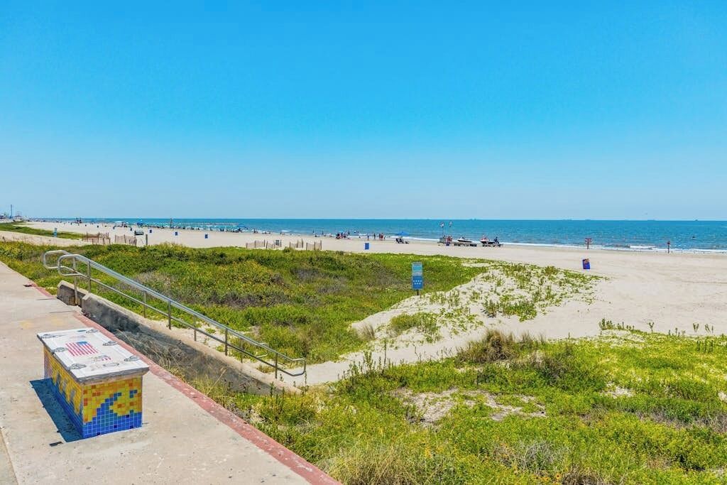 A beach with a walkway, a small kiosk, and a clear sky.