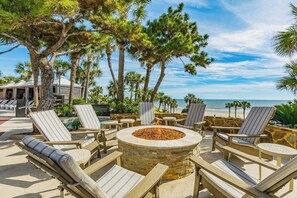A beachfront patio with lounge chairs, a stone fire pit, and a view of the ocean. - Gone Gulfin' - Gulf-Front Resort, Pool & Hot Tub (Galveston)