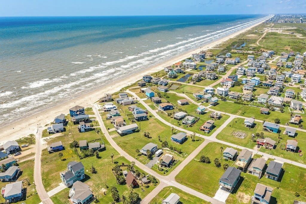 A coastal residential area with houses arranged in a grid pattern, a beach, and the ocean in the background.