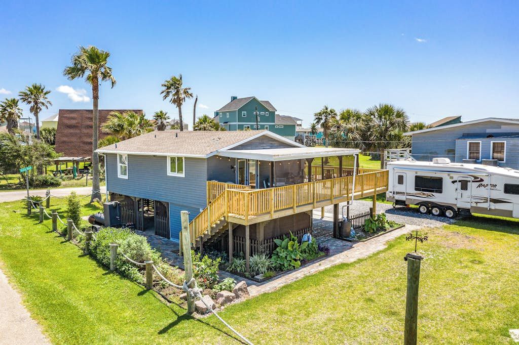 A single-story house with a covered porch and a small deck, surrounded by a well-maintained lawn and palm trees.