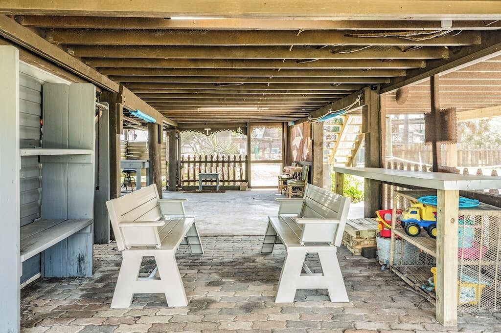 A covered outdoor seating area with benches and a table, surrounded by a wooden fence and a window with a view.