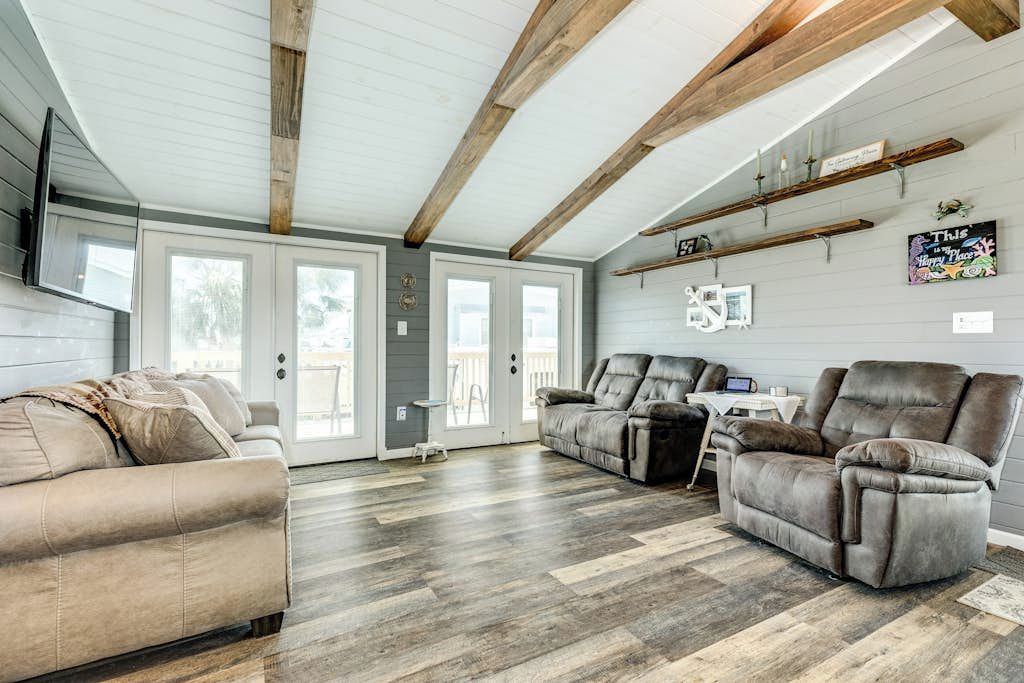 A spacious living area with a wooden ceiling, a grey sofa, a reclining chair, and a dining table.