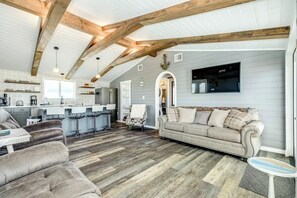 Ein großzügiger Wohnbereich mit hohen Decken, freiliegenden Holzbalken, einem grauen Sofa und einer Küche im Hintergrund.