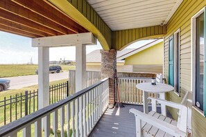 A covered porch with a stone pillar, a table, and chairs. - Craftsman on Seawall (Galveston)
