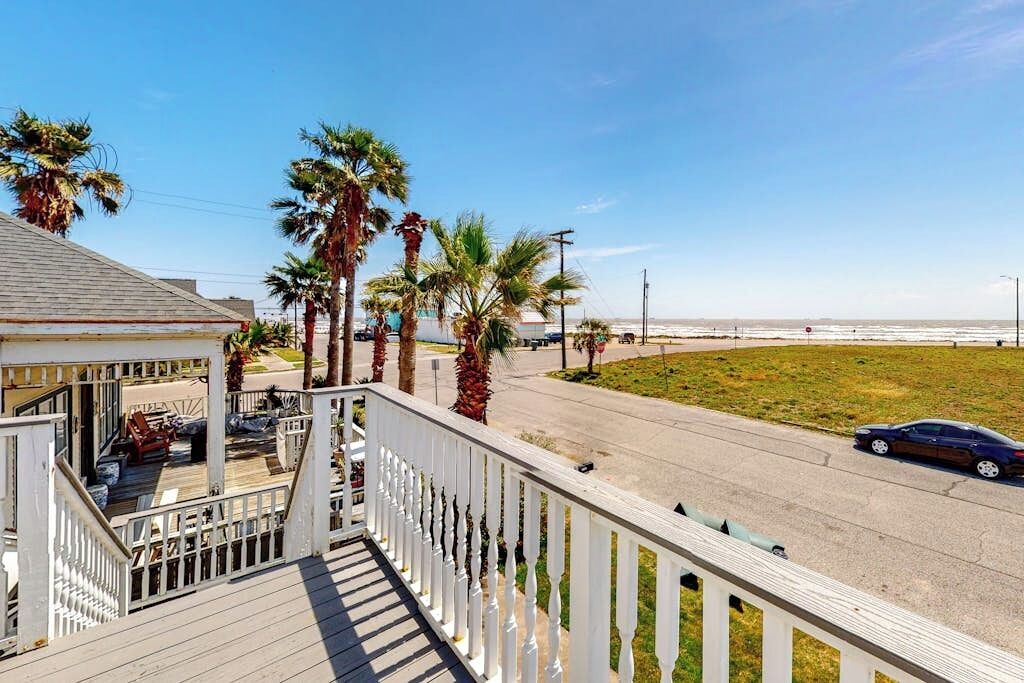 A coastal property with a wooden deck, palm trees, and a view of the beach.