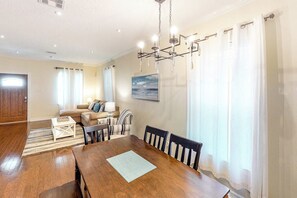 A dining area with a wooden table and chairs, a sofa, and a chandelier. - Craftsman on Seawall (Galveston)