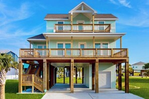 A two-story beachfront house with a wooden deck and a covered entryway. - The Green Palm - Bay-View Patio & Shared Pool (Galveston)