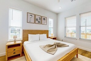 A bedroom with a wooden bed, white bedding, and two framed pictures on the wall. - The Green Palm - Bay-View Patio & Shared Pool (Galveston)