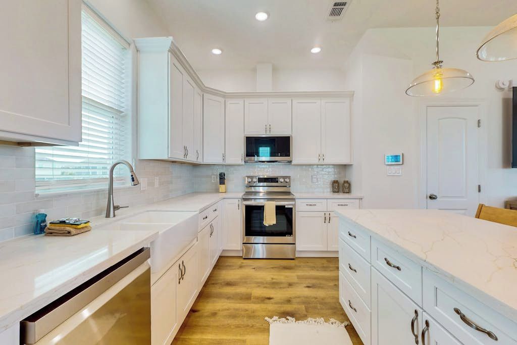 A modern kitchen with white cabinetry, stainless steel appliances, and a marble countertop.
