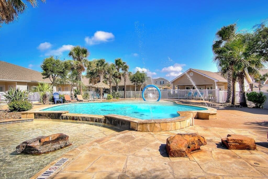 A swimming pool with a water slide, surrounded by palm trees and a clear blue sky.