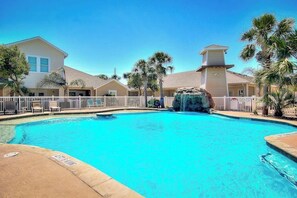 A swimming pool with a waterfall feature, surrounded by a fence, and adjacent to a building with a flat roof. - Palm Bay 306 - Pool & Patio, Short Walk to Beach (Corpus Christi)