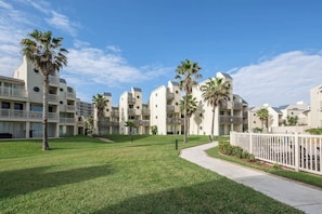 A residential building with multiple balconies, a well-maintained lawn, and a clear sky. - Solare Garden Villa 679F (South Padre Island)