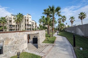 A pathway leading to a building with a stone wall, palm trees, and a wooden fence. - Solare Garden Villa 679F (South Padre Island)