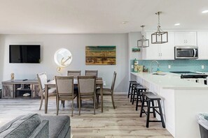 A modern kitchen with white cabinetry, a built-in microwave, and a bar area with stools. - Solare Garden Villa 679F (South Padre Island)