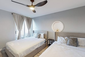 Ein Doppelbett mit Kopfteil, Nachttisch, Deckenventilator und Fenster mit Vorhängen.