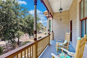 A porch with a wooden railing, a hanging lantern, and two rocking chairs. - Under the Avenue - Near the Beach & The Strand (Galveston)