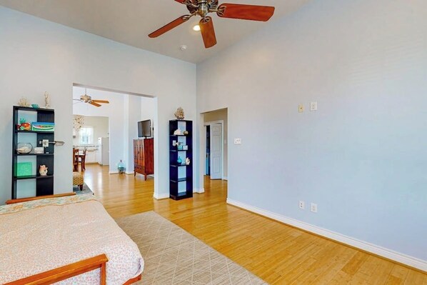 A spacious room with a bed, wooden flooring, ceiling fans, and built-in shelving units. - Under the Avenue - Near the Beach & The Strand (Galveston)