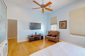 Una camera da letto con un letto, un ventilatore a soffitto, una televisione, una sedia e una finestra con persiane.