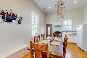 A dining area with a wooden table and chairs, a kitchen in the background, and a decorative wall piece. - Under the Avenue - Near the Beach & The Strand (Galveston)